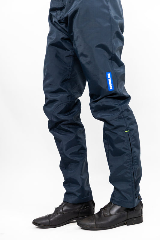 A pair of navy blue waterproof horse riding trousers with a neon yellow Velcro waist adjustment and a small brand tag on the left leg.